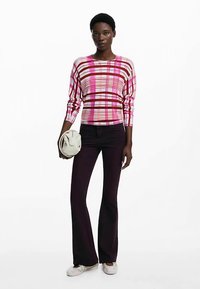 Dugotrajni višebojni prugasti top u ružičastoj i bordo boji, uparen s tamnoljubičastim zvonoliki hlačama i bijelim cipelama, držeći kremastu torbu.