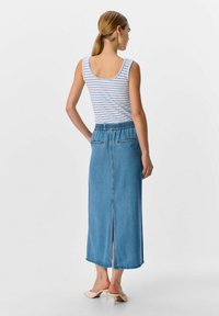 Jupe maxi en denim avec une taille élastique, couleur bleu clair, détail de fente arrière et deux poches arrière. Associée à un débardeur à rayures.