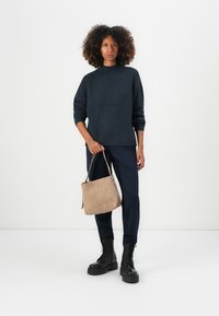 Pulover tricotat cu nervuri bleumarin, poșetă din suede bej, pantaloni bleumarin, bocanci negri cu șireturi. Ținută casual cu texte și culori variate.