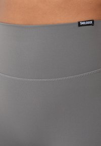 Leggings sportivi grigi con una texture liscia, dotati di una vita larga e cuciture a contrasto. Un'etichetta del marchio è visibile nella parte superiore.