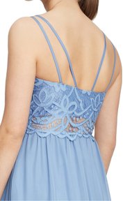 Světle modré šaty s krajkovými detaily na zádech, zdobené jemnými květinovými vzory, tenkými ramínky a splývavou sukní.