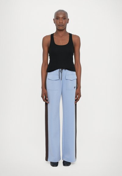 Top negro sin mangas, pantalones de pierna ancha de color azul claro con dos bolsillos frontales, franjas laterales marrones y cintura con cordón. Textura suave y ajuste relajado.