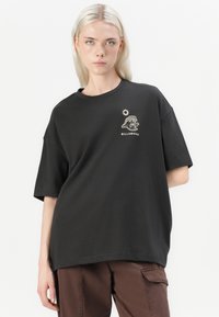 Black oversized t-shirt in soft cotton with short sleeves, featuring white embroidered graphics of a sun and a figure on the chest.