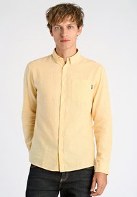 Lichtgele overhemd met lange mouwen, gemaakt van een gemengde katoenen stof met textuur, voorzien van een borstzak en een klassieke kraag. Gepaard met donkere jeans.