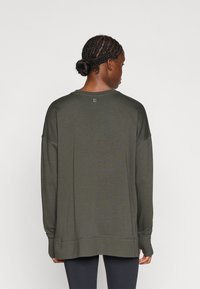 Sudadera de manga larga en tejido verde oscuro. Cuenta con un ajuste relajado, cuello redondo y detalles de costura a lo largo del dobladillo y los puños.