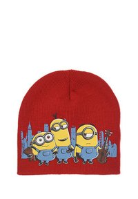 Berretto lavorato a maglia rosso con tre minion dei cartoni animati in tute blu, uno dei quali tiene un peluche, sullo sfondo di uno skyline cittadino.