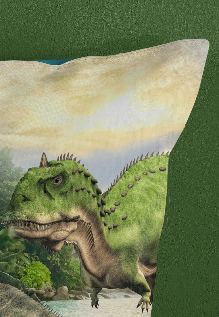 Die Illustration von dem grünen Dinosaurier zeigt eine schuppige Textur, stachelige Details und einen natürlichen Landschaftshintergrund. Der Kissenbezug hat eine weiche Stoffoberfläche.