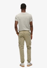 Lichtgrijs T-shirt met korte mouwen en beige cargopantalons met elastische boorden, voorzien van zijzakken en een relaxte pasvorm. Witte sneakers met zwarte accenten.