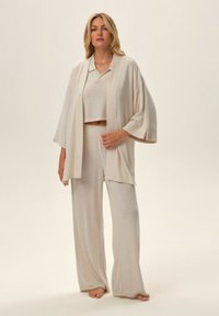 Beżowy zestaw odzieży domowej składający się z luźnego kardiganu, krótkiego topu i spodni o szerokich nogawkach, wykonany z miękkiego, lekkiego materiału.