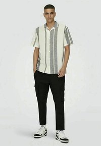 Chemise à manches longues avec des rayures verticales grises et blanches ; assortie à un pantalon cargo noir et des baskets noir et blanc. Design simple et décontracté.
