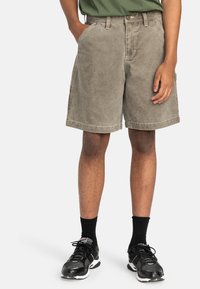 Pantaloni cargo kaki in cotone, con una vestibilità comoda, tasche laterali e orlo risvoltato. Indossati con scarpe sportive nere e calze.
