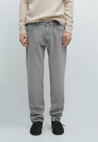 Light gray jeans with a loose fit, five pockets, and subtle stitching details, paired with black lace-up shoes.