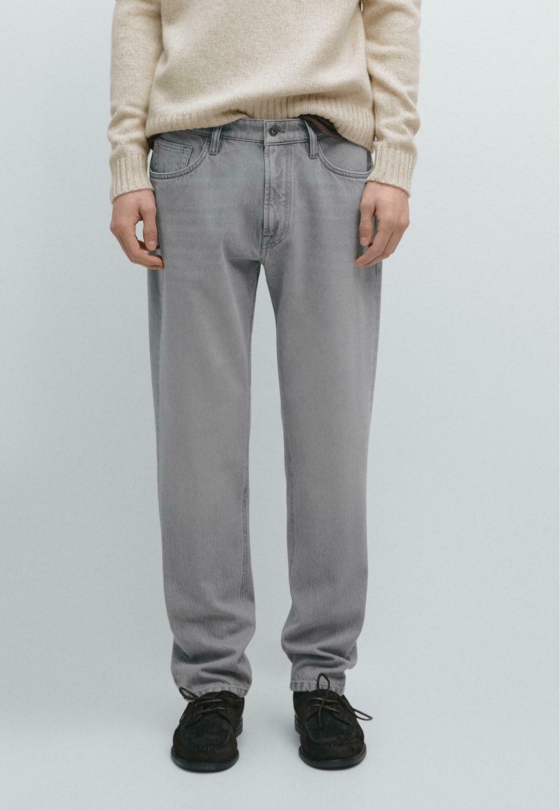 Light gray jeans with a loose fit, five pockets, and subtle stitching details, paired with black lace-up shoes.