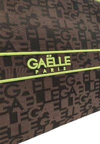Borsa di tessuto marrone con un motivo in rilievo del logo. Presenta una striscia di accento verde brillante e le parole "GAËLLE PARIS" in verde.