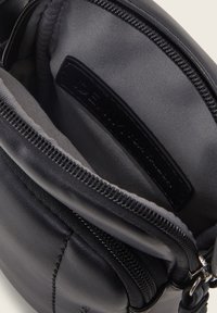 Interno di una borsa a tracolla in pelle nera con una consistenza liscia, caratterizzato da un comparto con zip e una fodera in tessuto. Contiene un'etichetta di marca.