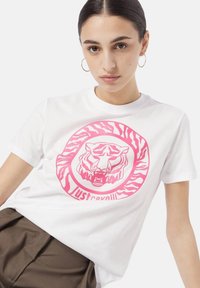 Hvid bomulds t-shirt med et stort pink tiger grafisk design med zebra-striber, suppleret af mærkenavnet "Just Cavalli" i fed skrift.