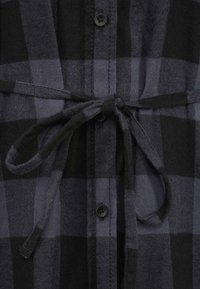 Camicia a quadri nera e grigia scura con cintura a cravatta, chiusura frontale con bottoni e tessuto testurizzato. Dettagli significativi includono bottoni neri e una finitura liscia.