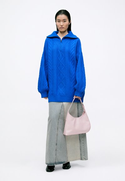 Suéter azul de gran tamaño, tejido, con un cuello alto y un patrón de diamantes. Combinado con una falda de mezclilla larga y un bolso rosa claro.