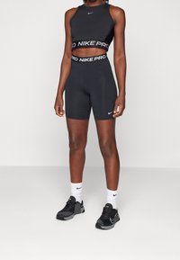 Czarny crop top Nike Pro z logo, zestawiony z czarnymi szortami o wysokiej talii. Całość uzupełniają czarne buty sportowe i białe skarpetki z logo.