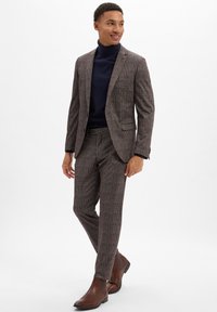 Braun kariertes Anzug mit taillierter Passform, kombiniert mit einem dunklen Rollkragenpullover und braunen Stiefeletten. Glattes Material und strukturierter Schnitt.