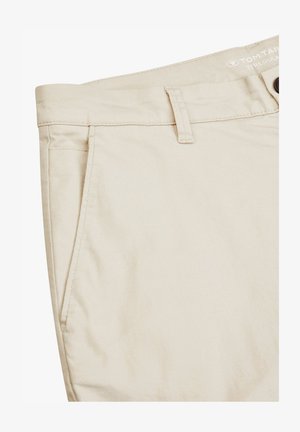 Pantalones de algodón beige con frente plano, bolsillos laterales y cierre de botón. Presentan una etiqueta con el logotipo y una textura sutil.
