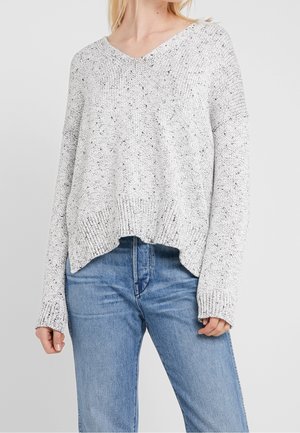Pull en maille gris clair moucheté avec col en V et manches longues porté avec un jean bleu sur une personne des épaules à mi-cuisse.