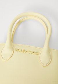 Gul lærveske med doble avrundede håndtak og preget "Valentino"-logo. Har en glatt tekstur og subtile sømmer.