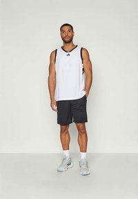 Weißes sportliches Tanktop mit schwarzen Akzenten, kombiniert mit schwarzen Shorts und hellgrauen Laufschuhen. Enthält das Adidas-Logo auf dem Oberteil.