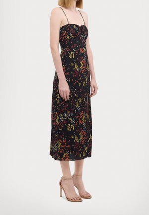 Robe noire à fleurs avec des motifs jaunes, rouges et blancs, longueur mi-mollet, fines bretelles spaghetti et corsage ajusté. Portée avec des talons nus à bride de cheville.