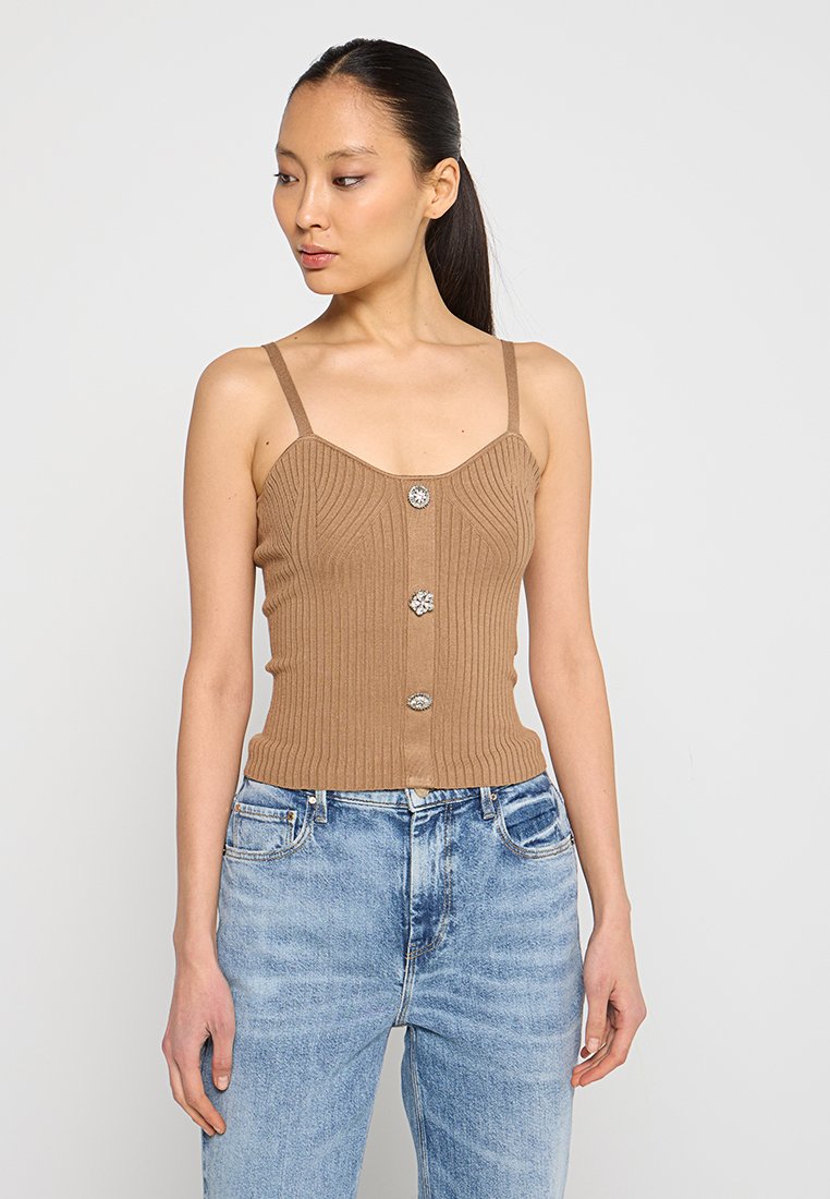 Beige Rippstrick-Top mit taillierter Passform und Knopfdetail in der Mitte. Dünne Träger und ein leicht strukturierter Stoff. Kombiniert mit blauen Jeans.