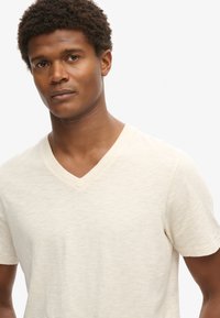 T-shirt a maniche corte con scollatura a V in bianco sporco, realizzato in tessuto morbido e testurizzato con un leggero motivo melange. Design minimalista, vestibilità casual.