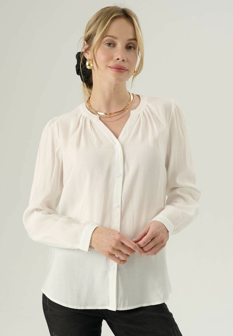 Bílé dlouhé rukávy blouse, lehký materiál, s knoflíkovým zapínáním vpředu, nařasenými rameny a zakulaceným lemem. Nosit s černými džíny.