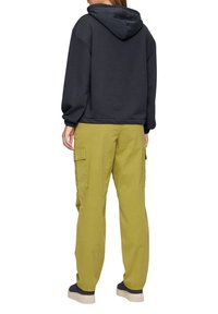 Hoodie oversize gris foncé avec une capuche à cordons, associé à un pantalon cargo vert olive clair avec des poches latérales et une coupe décontractée.
