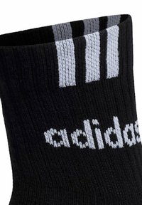 Czarna sportowa skarpeta o prążkowanej fakturze, z trzema szarymi paskami u góry i białym logo „adidas” po boku.
