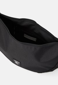 Black Lacoste zippered pouch open, showing empty interior and brand label on front and inside pocket.