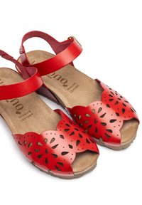 Red leather sandals with cut-out floral design, open toe, and ankle strap. Soft brown footbed with printed branding. Lightweight sole.