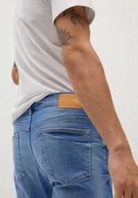 Jeans de mezclilla azul claro con acabado desgastado, diseño de cinco bolsillos y una etiqueta de cuero marrón en la cinturilla. Textura suave y corte ajustado.