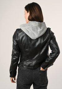 Schwarze Lederjacke mit grauem Kapuzenansatz, mit figurbetontem Design, Nahtdetails und Druckknopfakzenten an der Taille, kombiniert mit dunklen Jeans.
