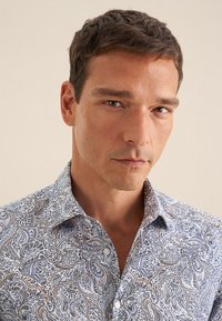 Koszula w jasnoniebieskim kolorze z misternym wzorem paisley w odcieniach granatowym i złotym. Posiada kołnierzyk z guzikami oraz teksturowany materiał.