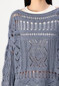 Light blue knitted sweater featuring openwork patterns, ribbed texture, and a loose fit with wider neckline and detailed design elements.