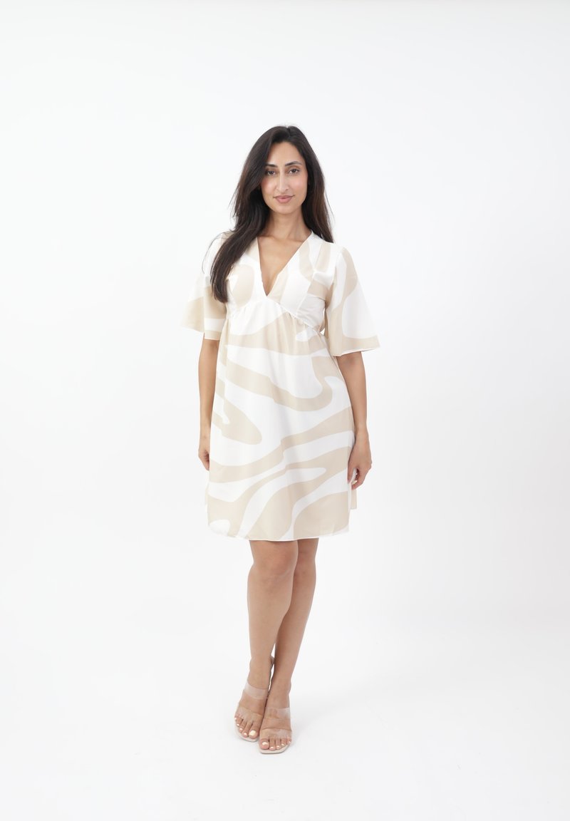 Vestido de manga corta y escote en V en color beige claro con patrones ondulados blancos. El tejido parece suave y ligero, alcanzando la mitad del muslo.
