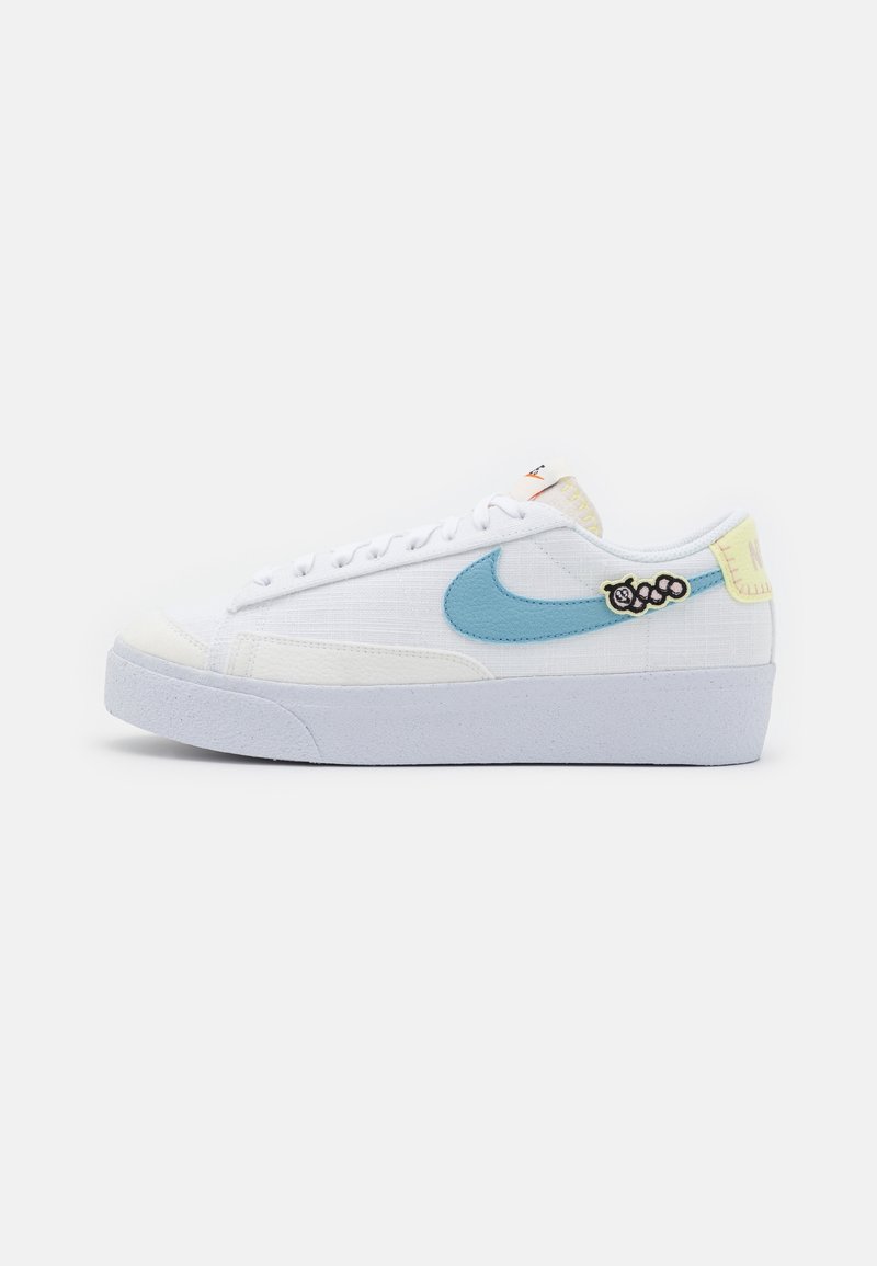 Baskets basses blanches avec un swoosh Nike bleu clair, languette de talon jaune pastel, petite pièce fleur noir et blanc, et semelle blanche.