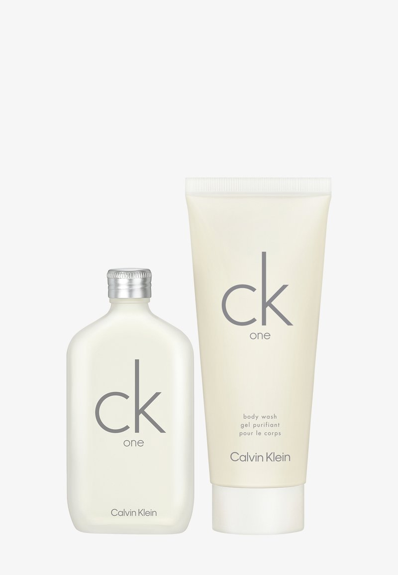 Set di bagnoschiuma Calvin Klein CK One, con una bottiglia trasparente e rotonda con tappo argento e un tubetto bianco con semplice testo grigio.