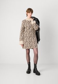 Vestido de suéter bege com um padrão de estampa de leopardo, com gola e punhos canelados, combinado com botas de tornozelo de couro pretas e uma jaqueta de couro.