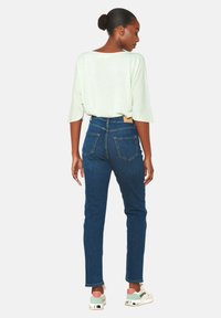 Šviesiai žalia tekstūruota viršutinė dalis su plačiomis rankovėmis, derinama su aukštu juosmeniu tamsiai mėlynomis džinsomis. Modelis vilki baltus ir žalius sportbačius.