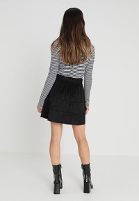 Mustat samettiset kerrokselliset hameet, joissa on joustava vyötärö, yhdistettyinä musta-valkoisiin raidallisiin pitkähihaisiin paitoihin ja mustiin korkokenkiin.