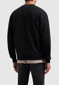 Zwarte sweatshirt met een ronde halslijn en geribde manchetten. Glad materiaal, aansluitend op de taille, gecombineerd met donkergrijze jeans.