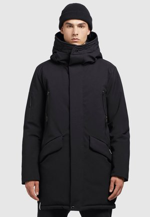 Parka negra con un alto cuello, bolsillos con cremallera y una capucha acolchada. Fabricada con un tejido resistente con un acabado mate.