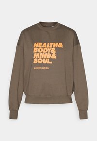 Hnedá mikina s dlhými rukávmi, okrúhlym golierom a rebrovanými manžetami. Má veľký oranžový nápis: "ZDRAVIE & TELLO & MYSEĽ & DUŠA." Značka BJÖRN BORG.