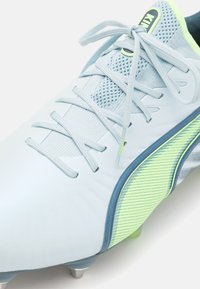 Botas de fútbol azul claro con material de malla y sintético, presenta acentos verdes, diseño texturizado y sistema de cordones tradicional con tacos.